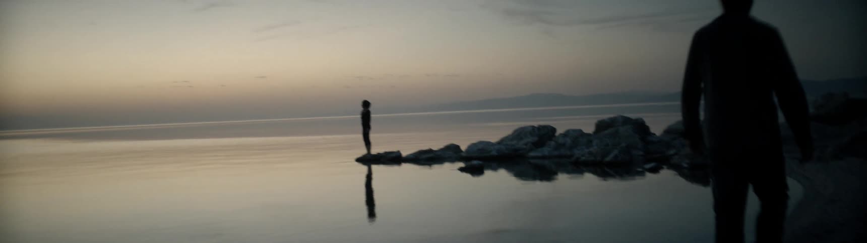 A person looks towards the sunset on the rocks by the shore