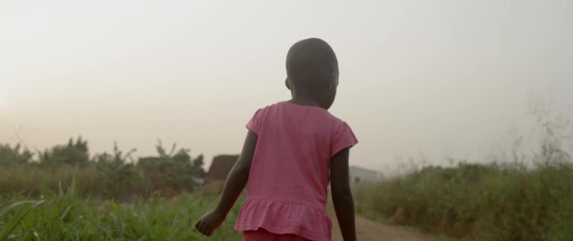 A girl walks on a dirt road and touches the grass on the side