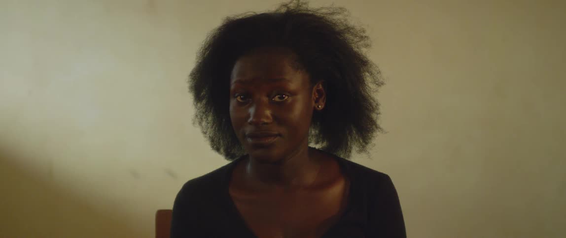 A woman sits at a chair and stares forward