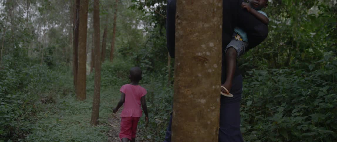 A man and two children walk on a small trail in the woods
