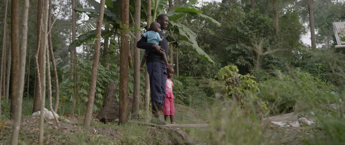 A man holds a young boy and stands with a young girl in the woods