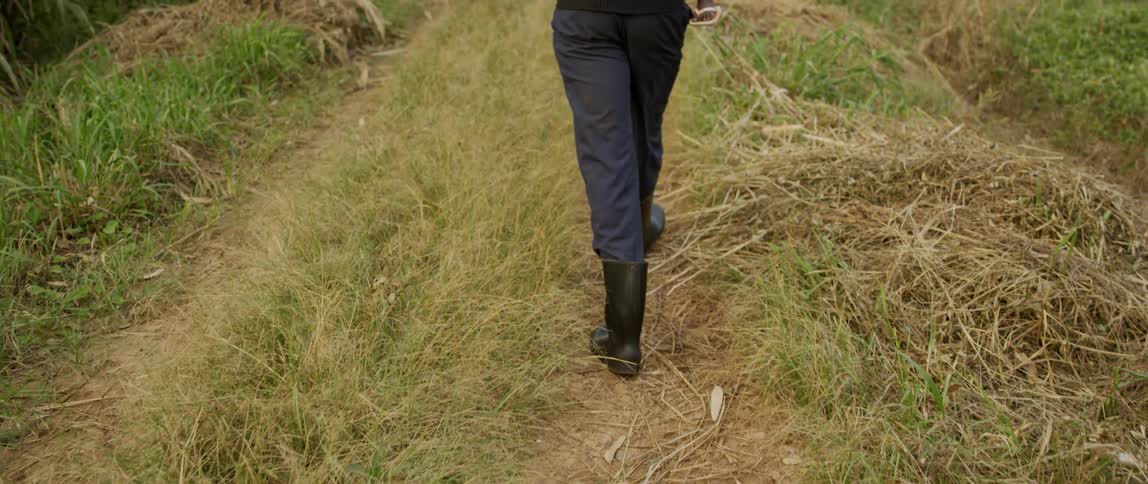 A man wearing boots and holding a child walks a grassy trail