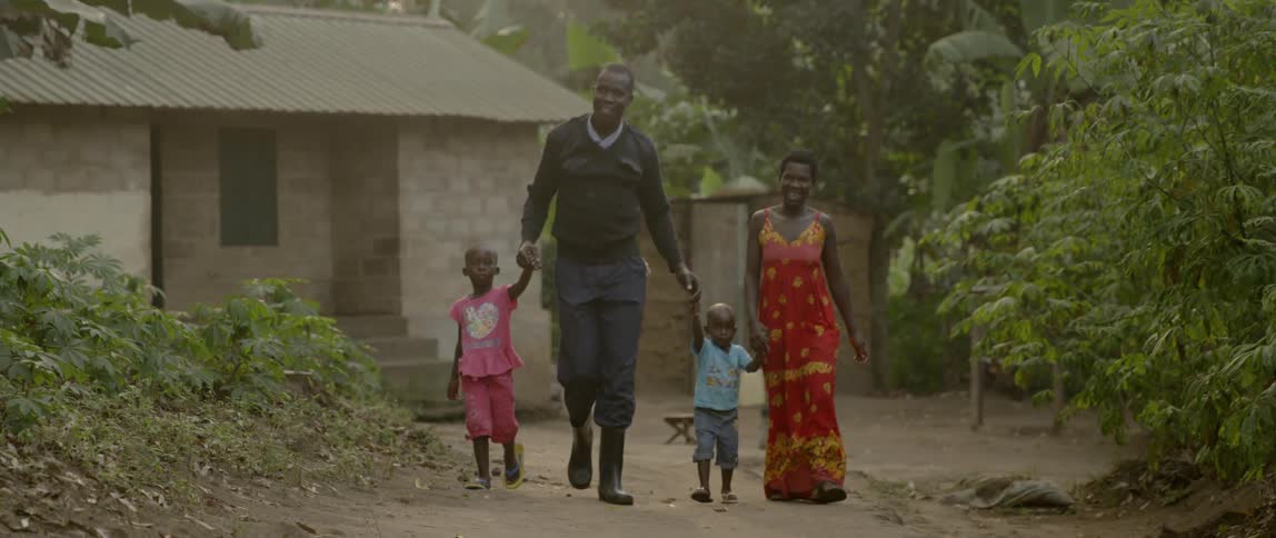 Parents hold their children's hands as they walk on a dirt road