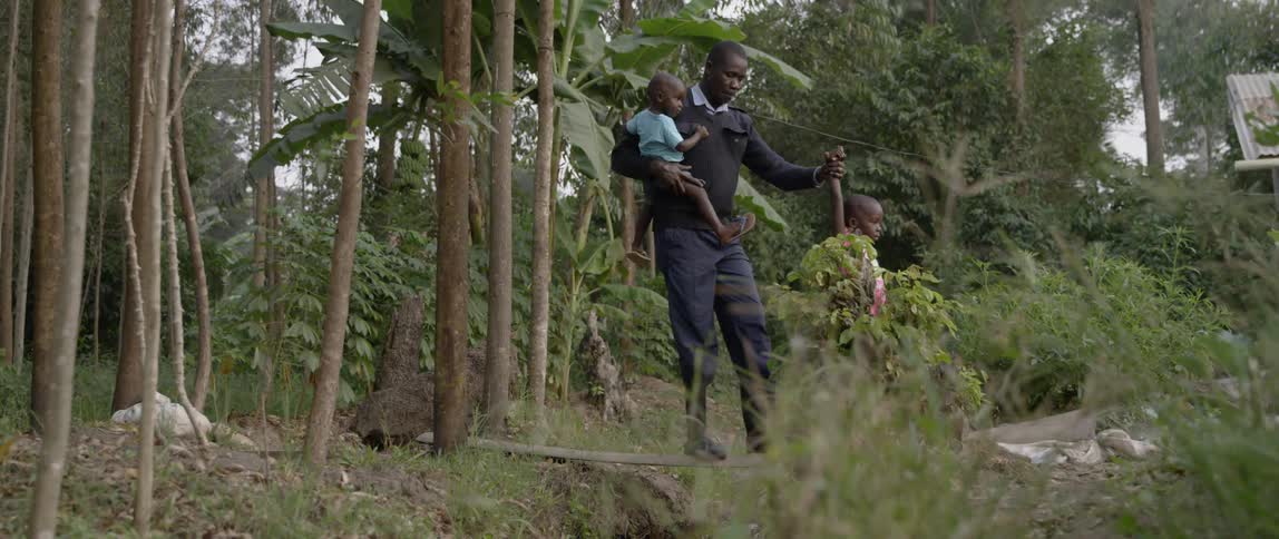 Man walking with two children over a plank that spans a shallow gorge in the forest