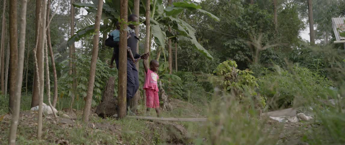 Man walking with two children over a plank that spans a shallow gorge in the forest