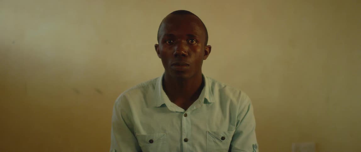 A man turns his head forward as he sits in front of a wall in daylight