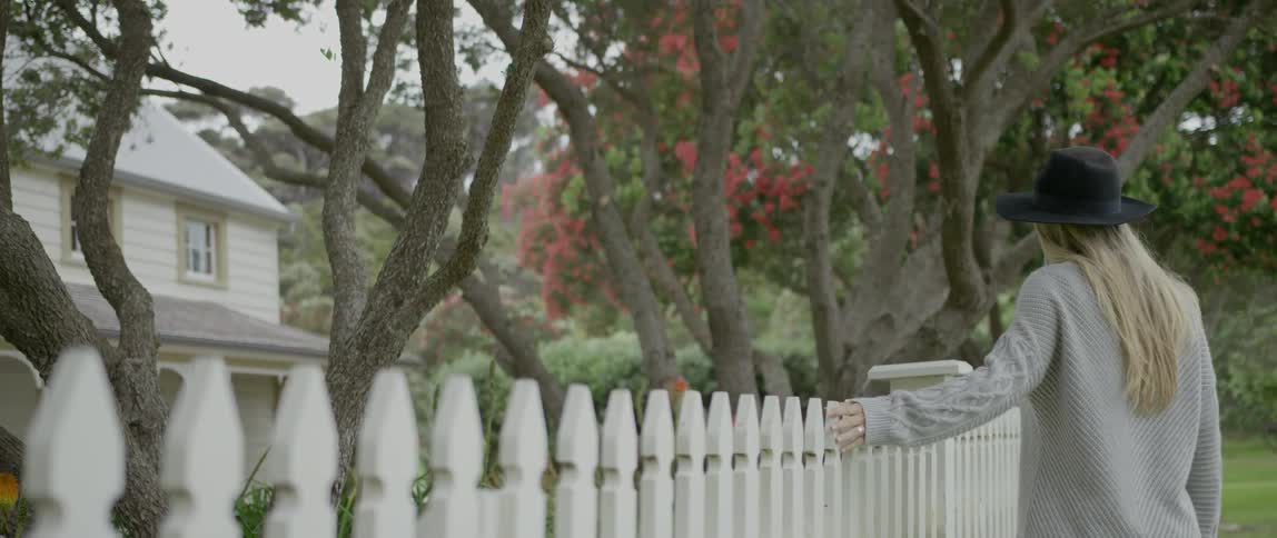 A woman runs her hand along a white picket fence