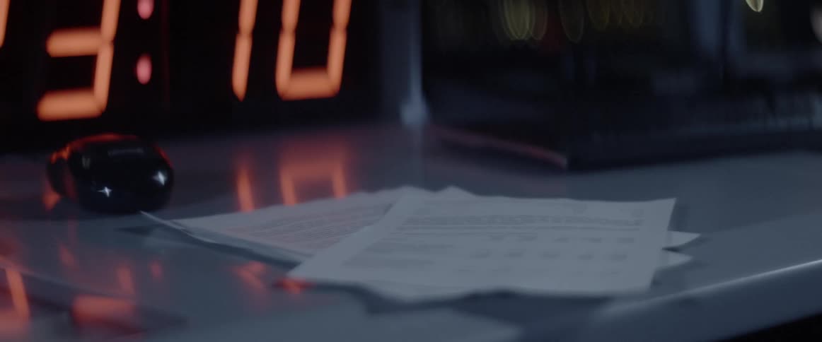 Papers fall into a pile on a desk by a clock