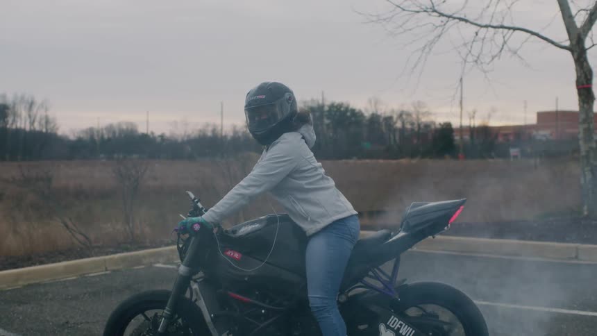 Someone is sitting on a motorcycle doing a burnout in a parking lot