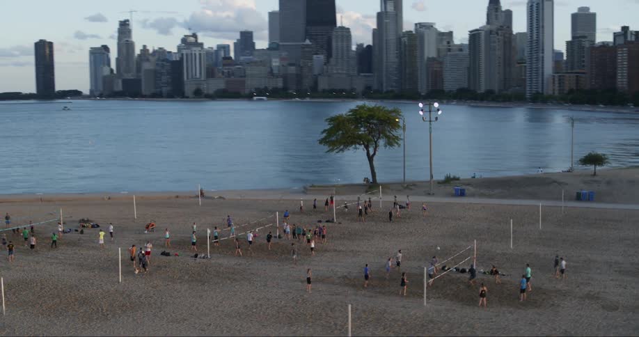 People re playing volleyball on the beach with a large city in the background
