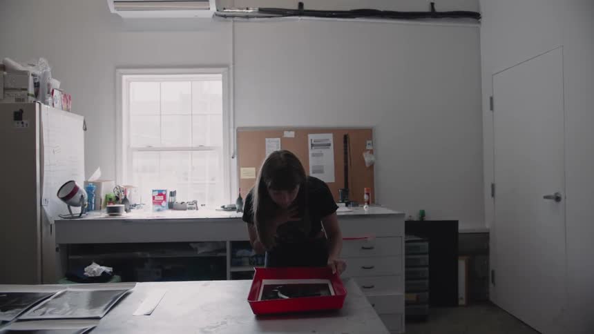 A woman looks at a photograph in a developing tray