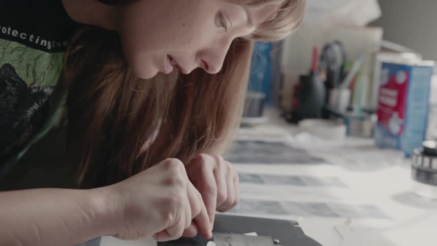 A woman leans over film negatives at a workbench