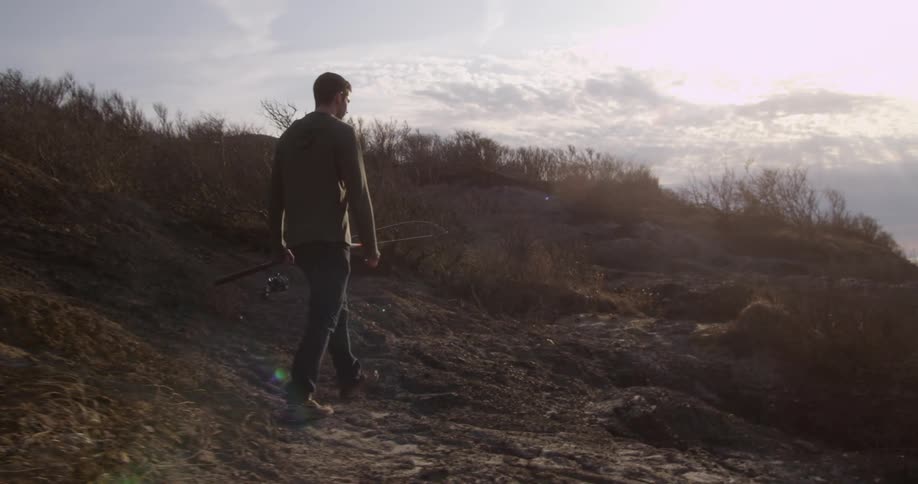 Man holding a fishing pole walks down a hill