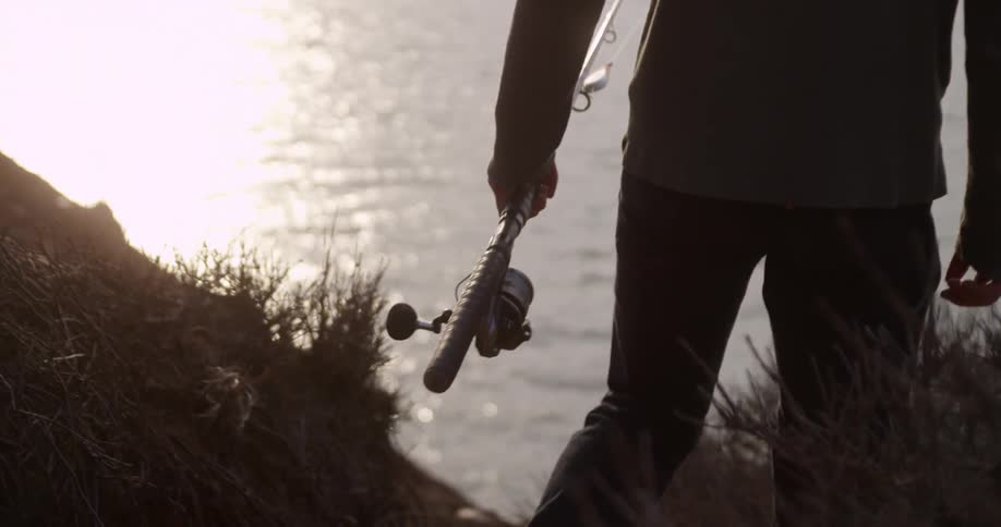 A man walks with a fishing pole towards the water