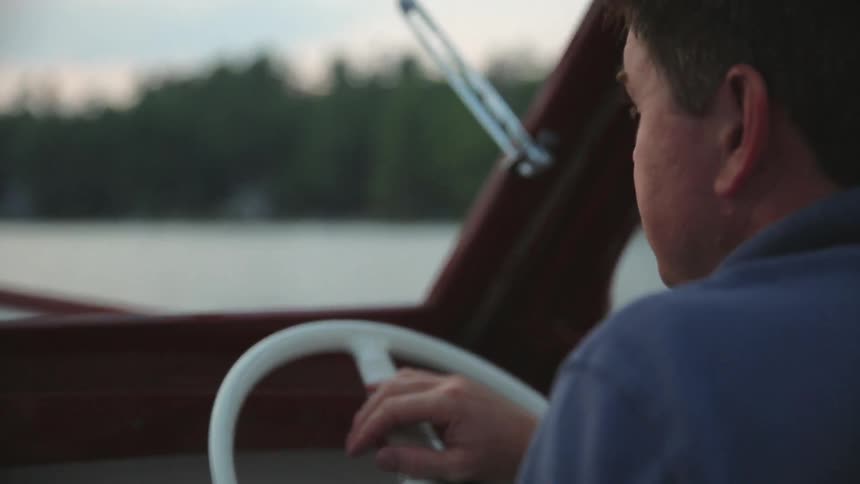 A white man steers a boat across a body of water