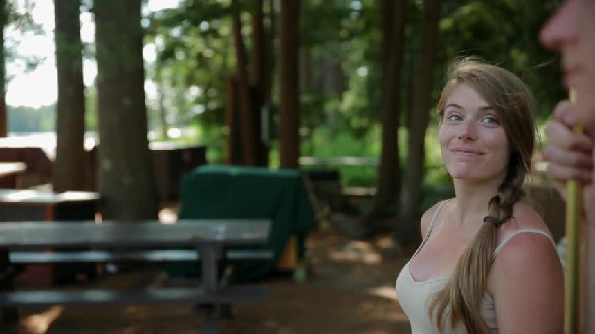 A young, blonde woman sitting on a picnic table bench turning to smile at a man