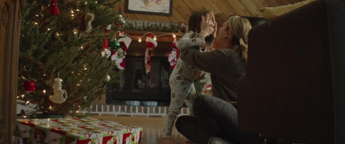 A woman kisses her daughter by a christmas tree