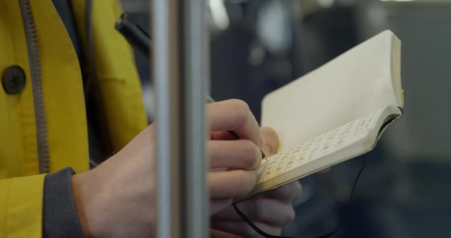 A man is listening to music and writing a note