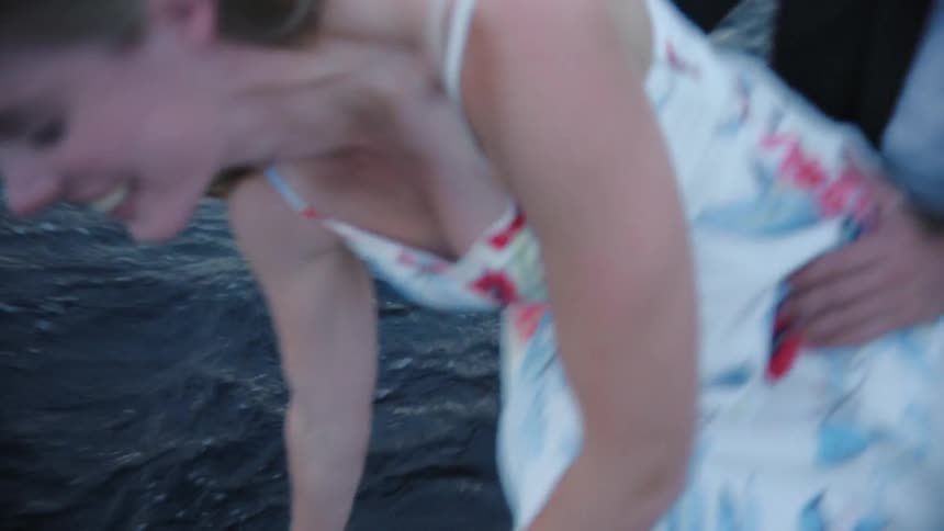 A white woman leans over the side of a boat to run her hand over the water and then kisses her husband
