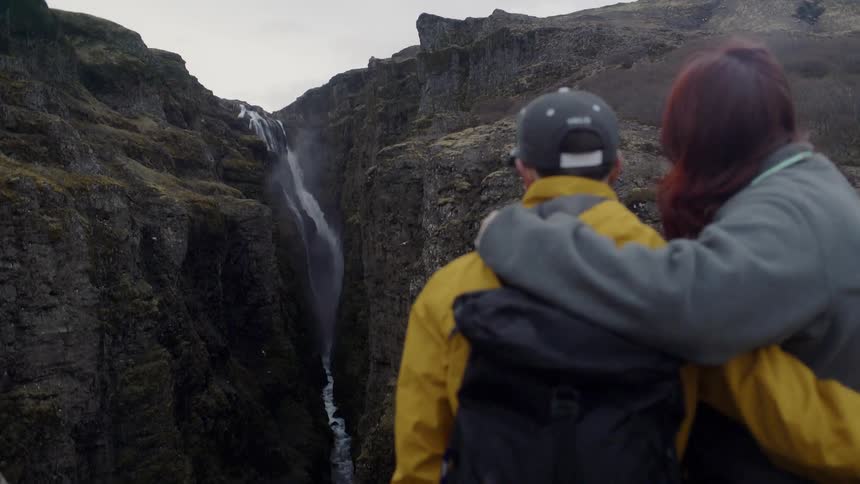 Man and woman embrace as they look at a large waterfall