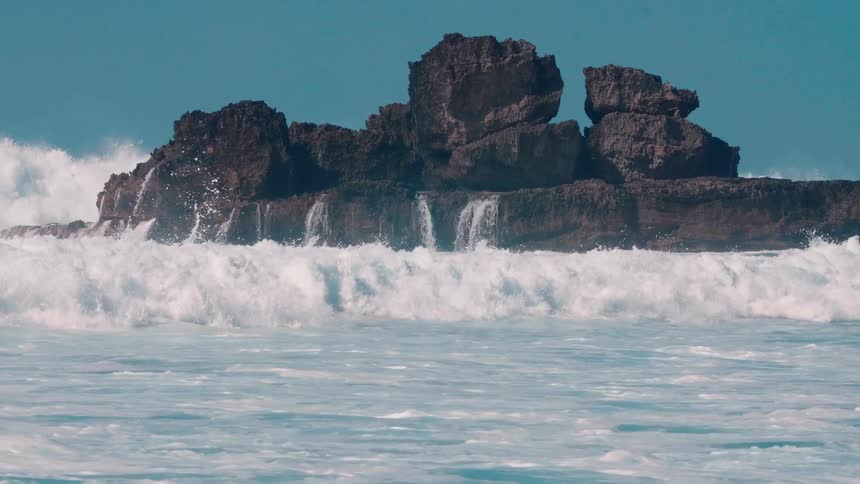 Waves splash up around a large rock formation
