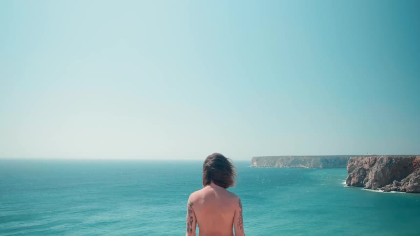 Man stands looking out over the ocean on windy day