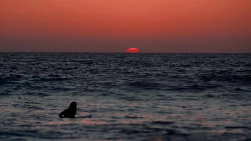 A surfer is floating on his surfboard as the sun sets