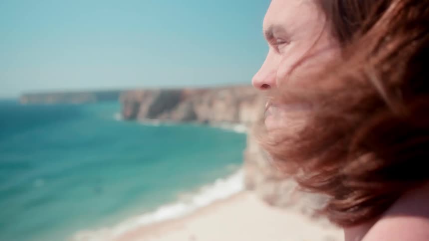 Man observing the ocean on sunny day while wind blows his hair