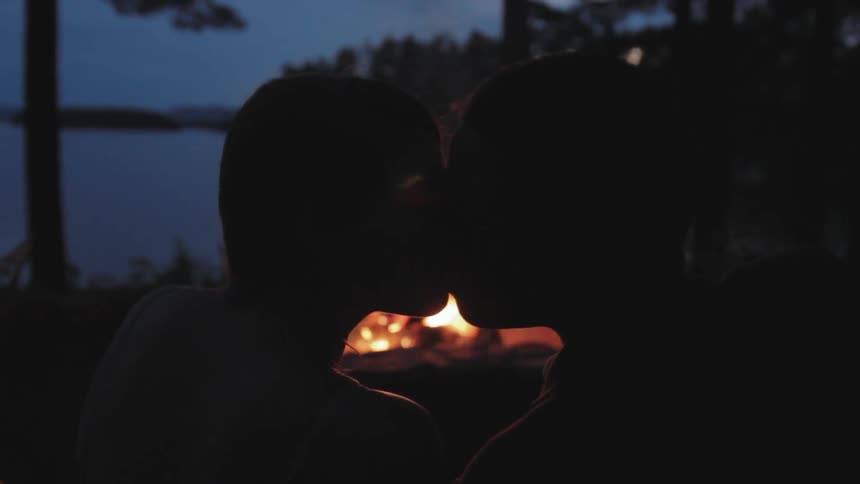 People kiss in front of a large campfire