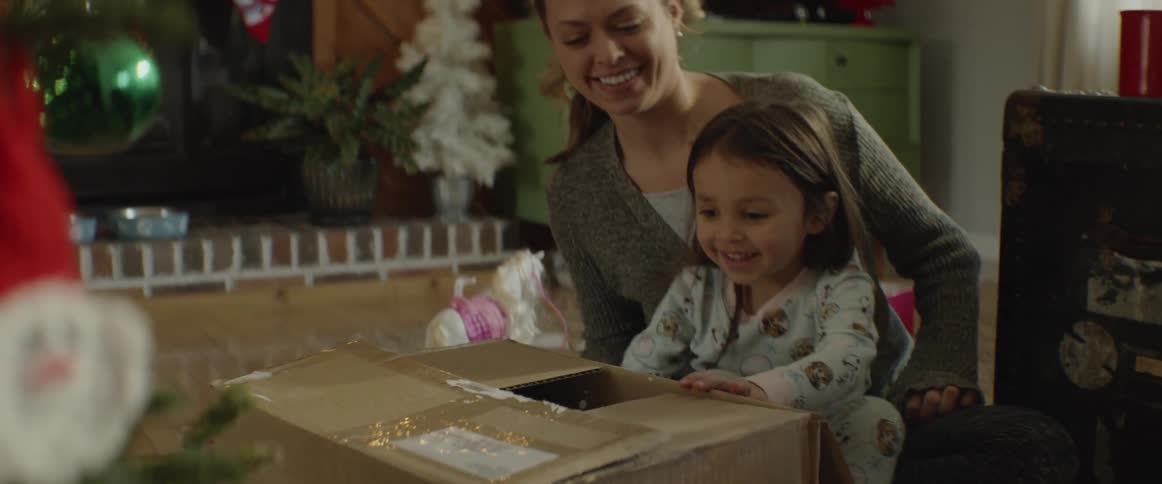 Daughter smiling and sitting on her mother's lap as she opens box