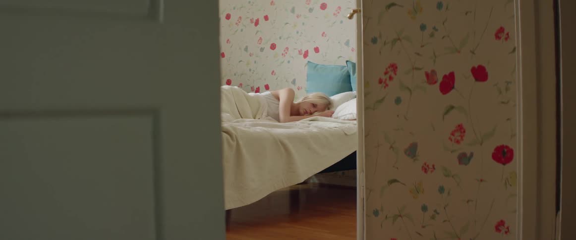 Blond woman starting to wake up in her bedroom that has floral wallpaper