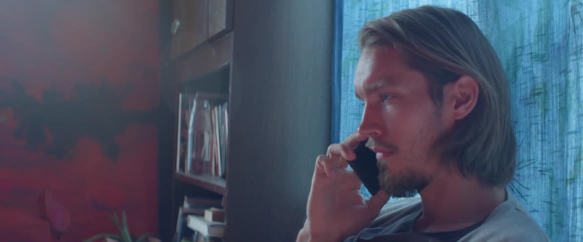 Profile view of a young man having a quiet smartphone conversation near window.