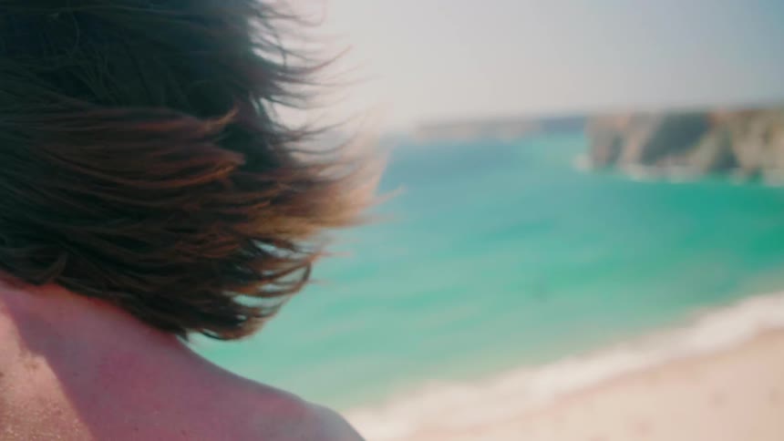 A woman stands on a beach on a windy day