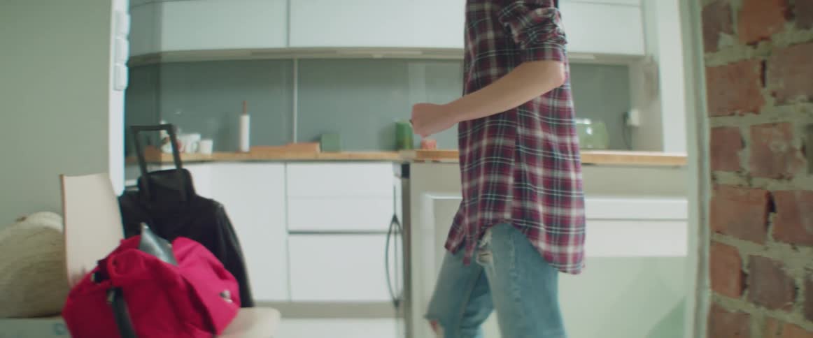 Mid section shot of a person in flannel walking past luggage at home.