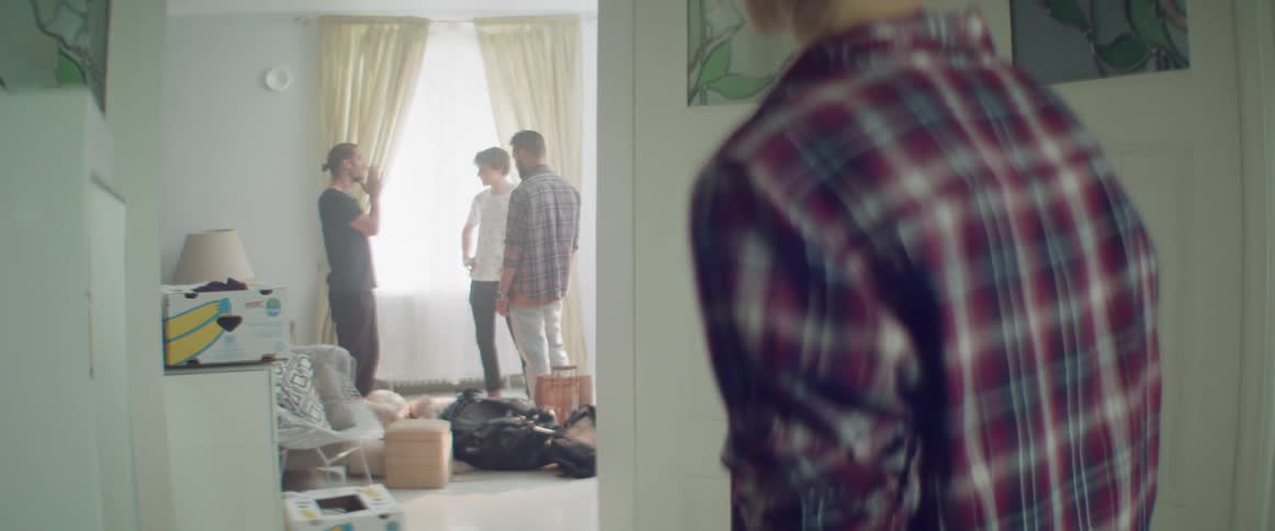 A young woman peeks from behind a corner at men chatting indoors.