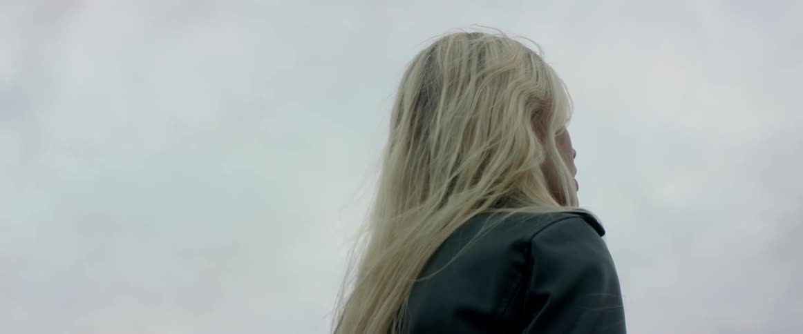 A thoughtful young lady wears a dark jacket while standing near the water.