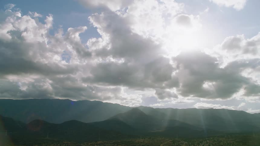 Sunlight is streaming through clouds over a desert road and hills during the day