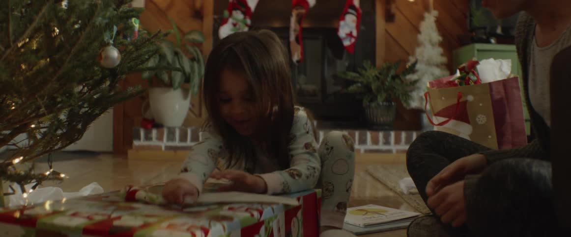 Mother sits by daughter as she opens christmas present