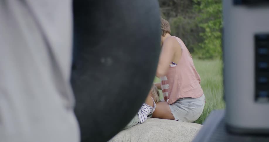 A mom plays with her daughter near the grass while dad picks up his son