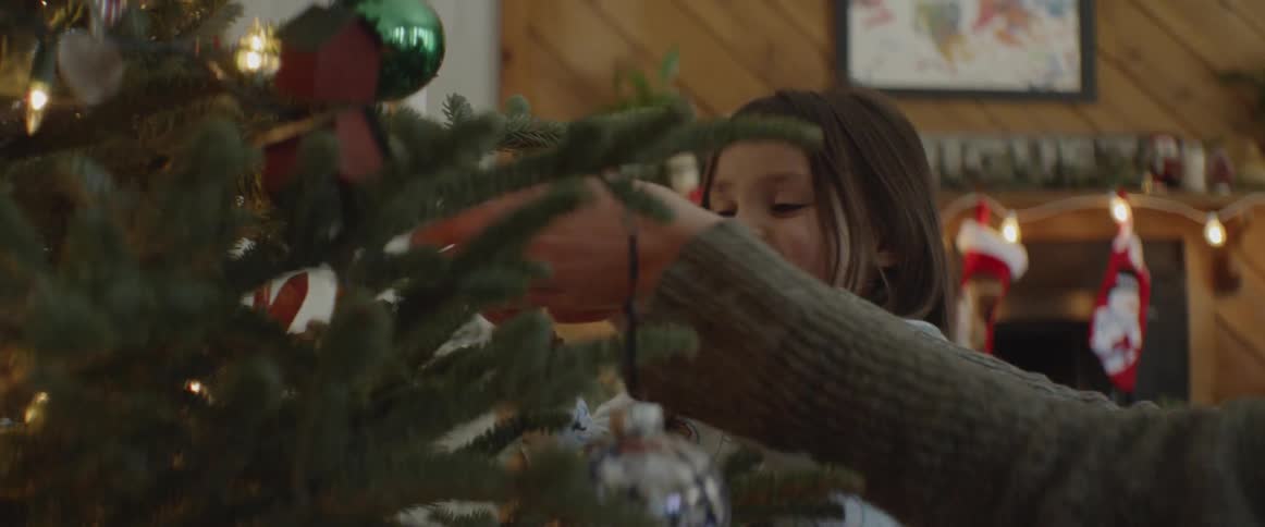 Little girl smiling while looking at ornaments on christmas tree