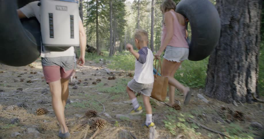 A family are hiking through the forest with some rafts to play in the creek