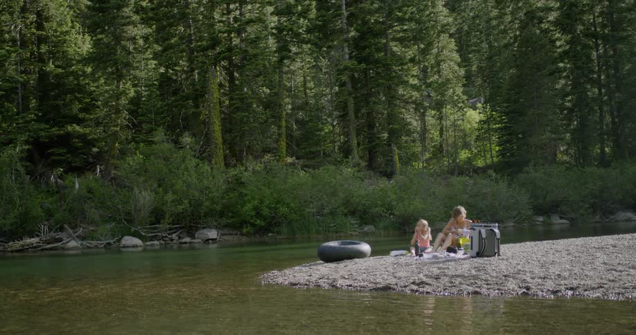 Mother and daughter having picnic next to river on sunny day