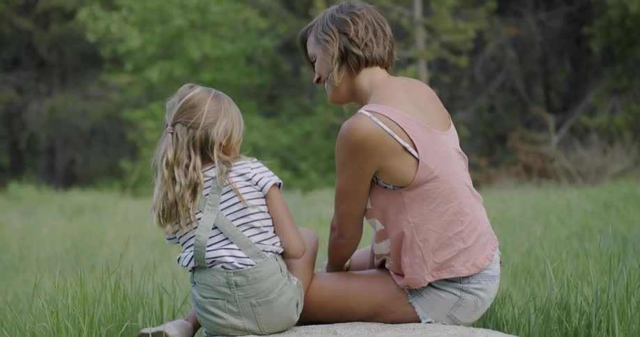 A mom and daughter sit in the grass and play