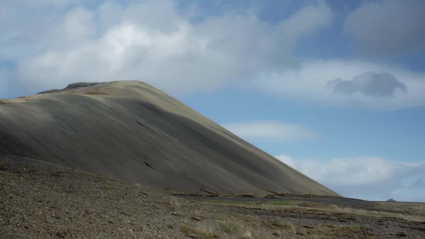 White clouds hang above a large hill