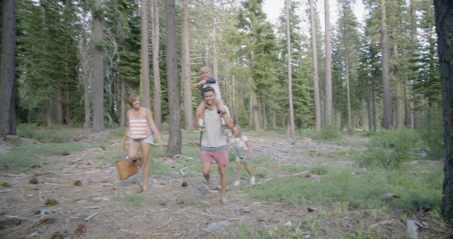A dad carries his son on his shoulders as the family walks through the trees
