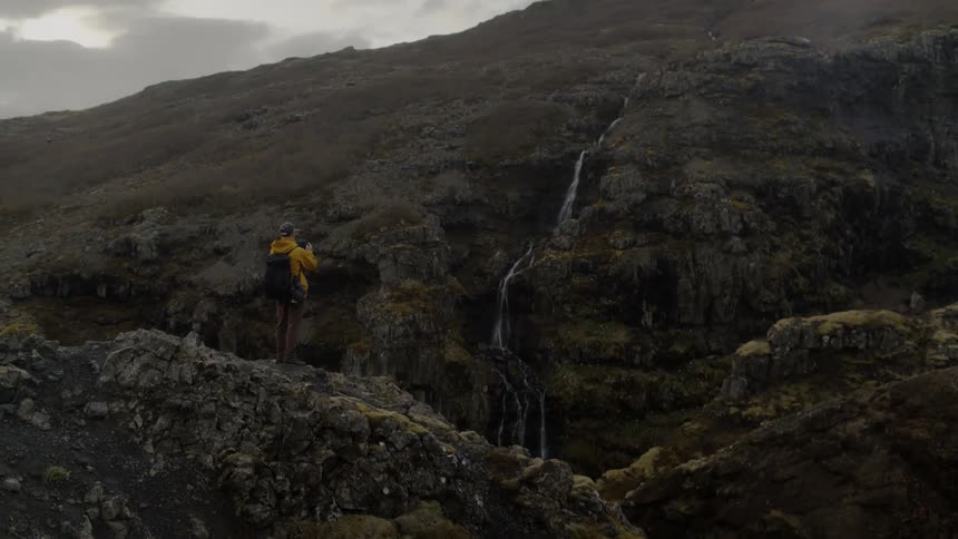 A man takes photos of a waterfall from a cliff