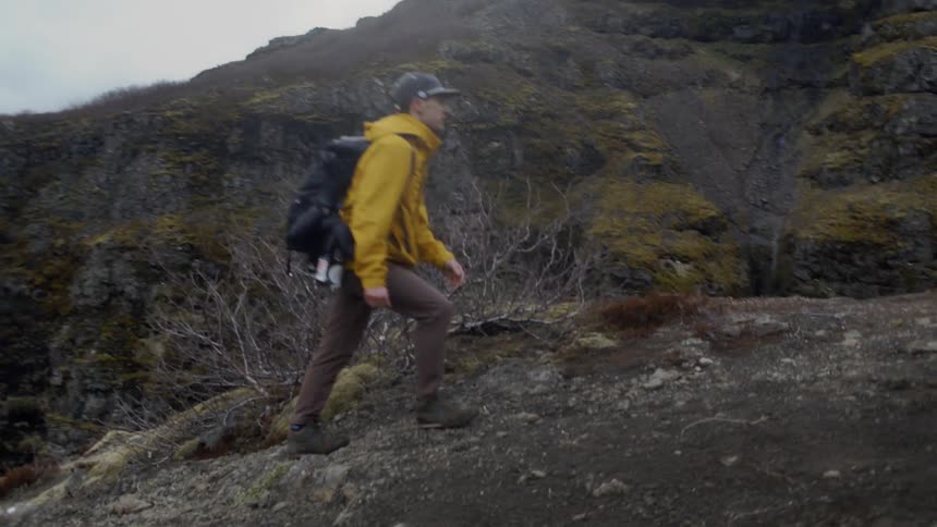 Man wearing backpack is hiking up a mountain on cloudy day