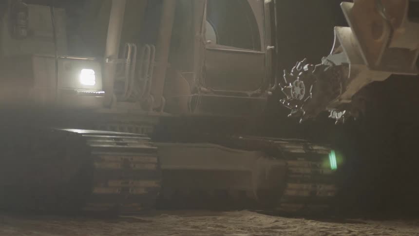 Tractor rolls over the land and shines its headlights at night
