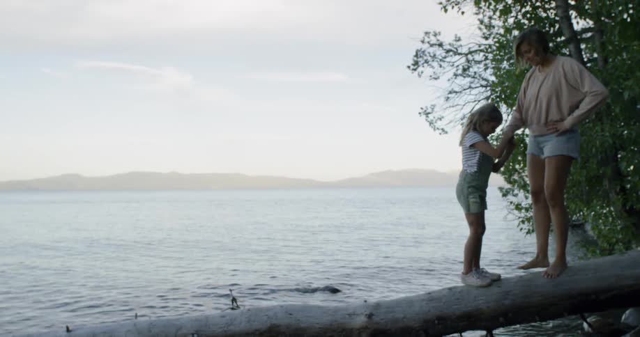 Mother and daughter play on log next to lake