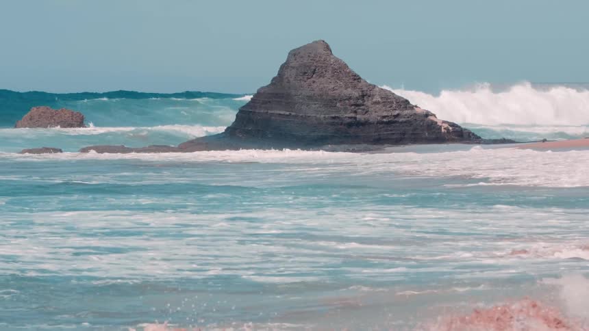 Blue ocean waves are crashing onto beach on sunny day